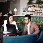 man in front of laptop with lady to the side at a cafe setting